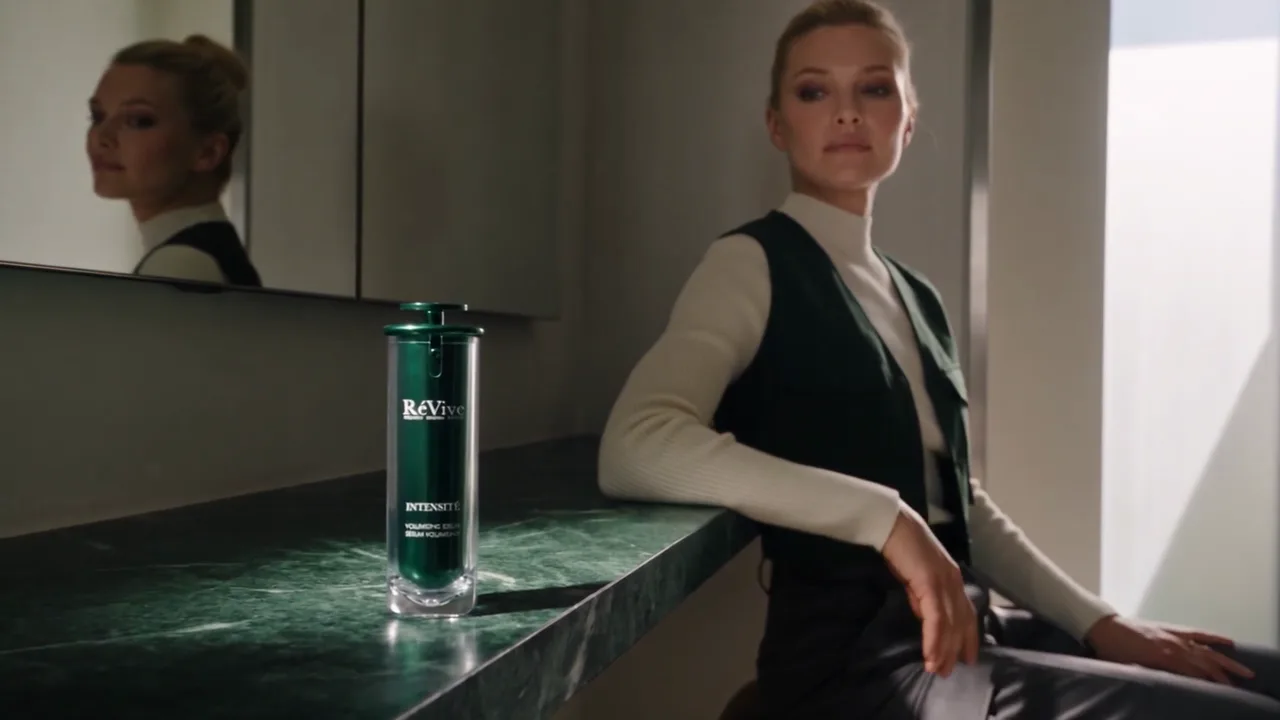 RéVive Intensité spec beauty film — a woman in a green vest beside the serum on a green marble counter, reflected in mirrors