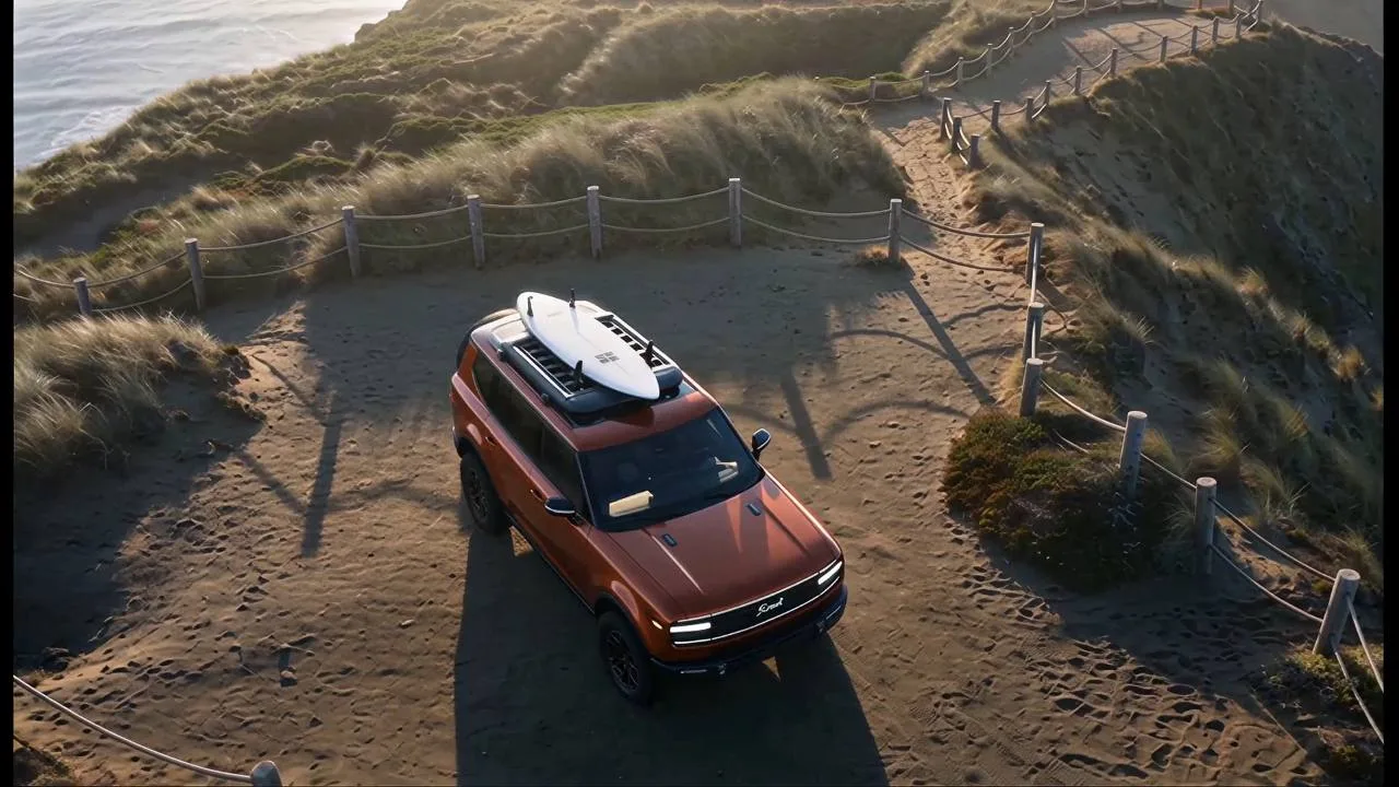 Scout Motors spec automotive film. An orange Scout Traveler parked on a coastal bluff with a surfboard racked on the roof, ocean below