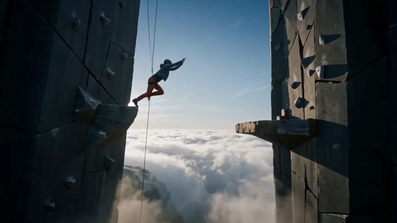Sutra V spec wellness film. A climber in rust-orange pants leaping the gap between two vast climbing towers above the clouds