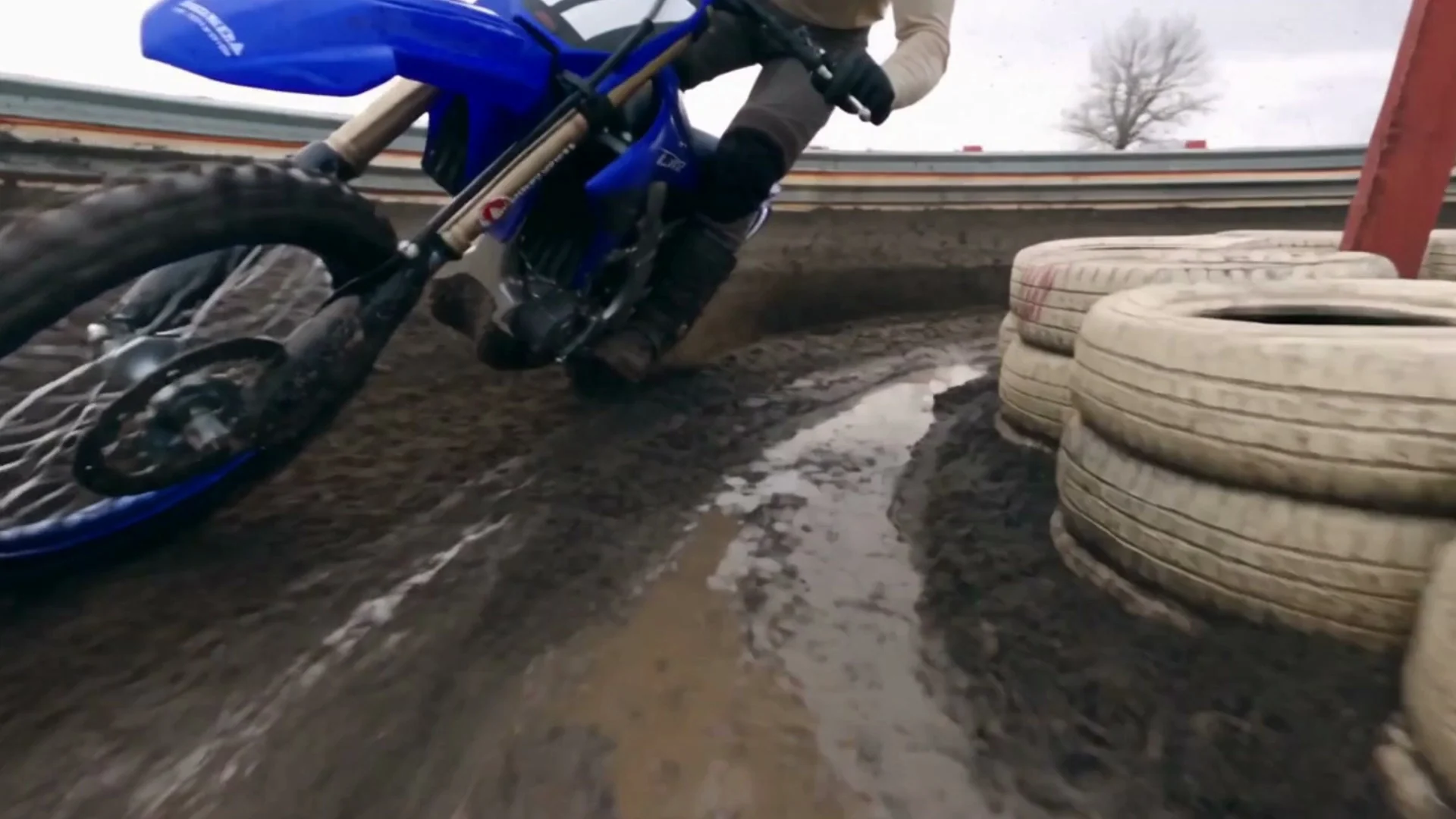 A low motocross shot through a muddy corner lined with tires, from a film made in Fotyra Studio